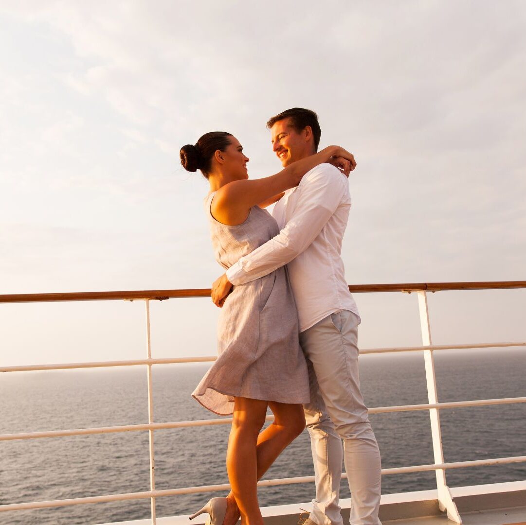 A young couple hugging on their holiday cruise, beside the balcony with the sea in the background.